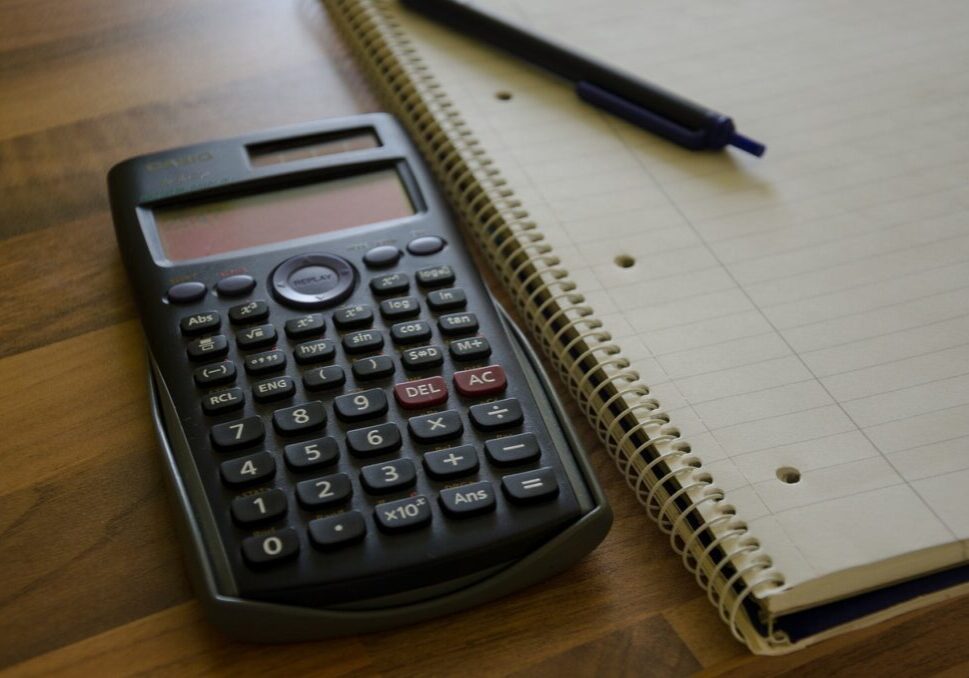 A calculator sitting next to an open notebook.